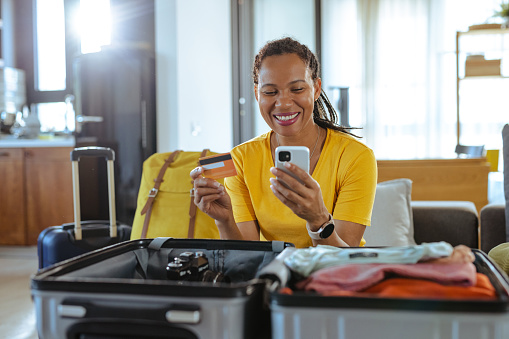 Mature African American woman packing for a trip and using online payment services