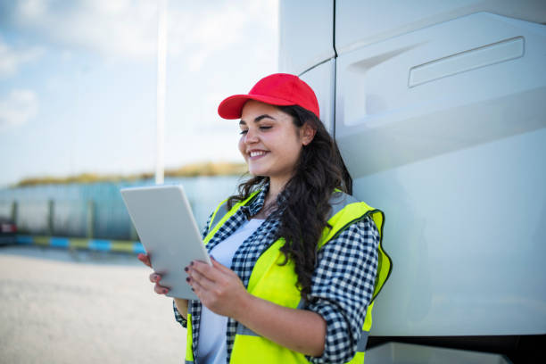 istock Smiling female trucker standing beside the truck and using technology. 1586242932