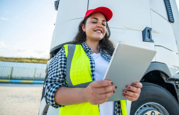 istock Smiling female trucker standing beside the truck and using technology. 1586242951