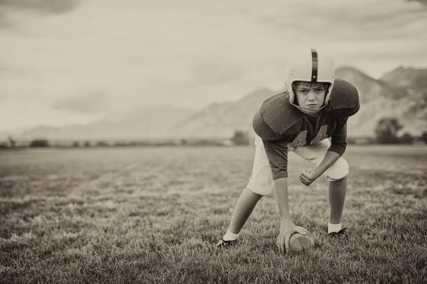 Football Time A young American Football boy is ready for the next play from the scrimmage line. Vintage theme. center athlete stock pictures, royalty-free photos & images