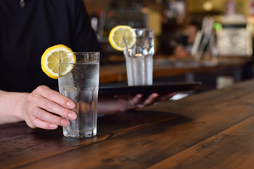 Restaurant server placing glass of cold water with lemon on a table