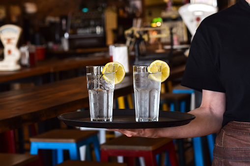 Restaurant server holding a tray with two glasses with cold water, ice and lemon slice