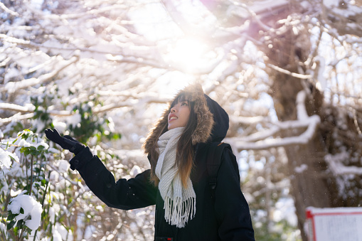 Young Asian woman in black coat looking beautiful nature in forest mountain covered in snow in snowy day. Attractive girl enjoy travel small village in Japan on holiday vacation in winter season.