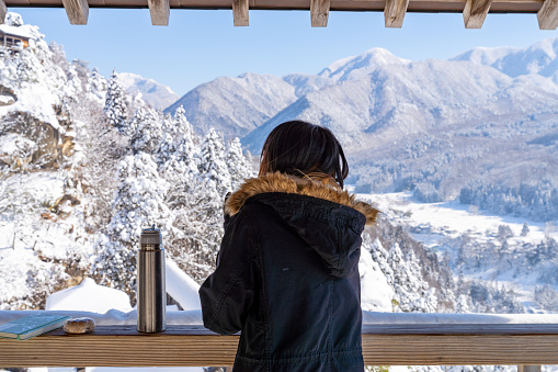 Young Asian woman relaxing at wooden seat and pavilion rest stop on the mountain during travel on road trip in Japan. Attractive girl enjoy outdoor lifestyle travel on holiday vacation in winter snow season