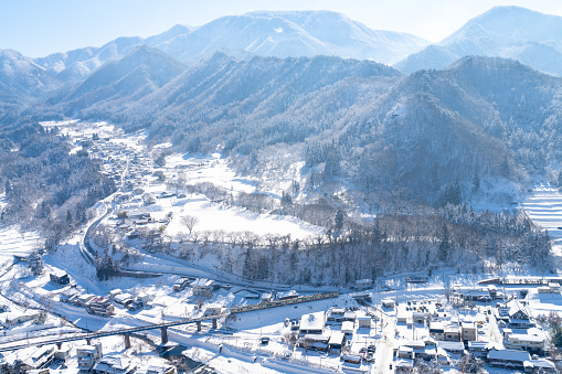 Drone Aerial view Landscape of Beautiful scenic nature in winter season with small village and river between the mountain in snowing day. Pine tree forest mountain and local road covered in snow.