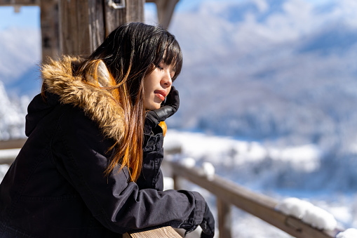 Young Asian woman relaxing at wooden seat and pavilion rest stop on the mountain during travel on road trip in Japan. Attractive girl enjoy outdoor lifestyle travel on holiday vacation in winter snow season