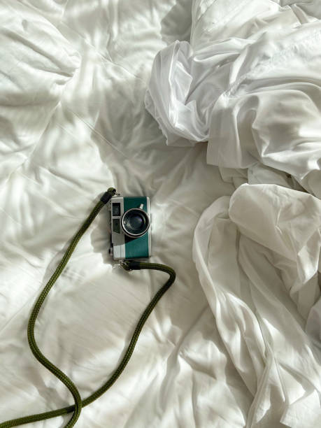 istock Vintage 35mm film camera rests on unmade bed sheets 1586442843