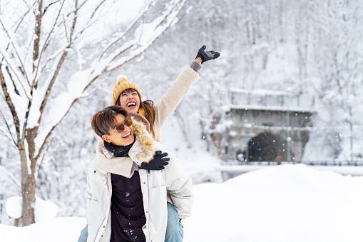 Asian couple playing together during travel forest mountain ski resort covered in snow on winter holiday vacation. Man and woman enjoy and fun outdoor lifestyle travel local town in Japan in snowy day