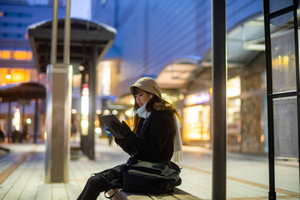 istock Asian woman working on digital tablet at bus stop. 1586458840