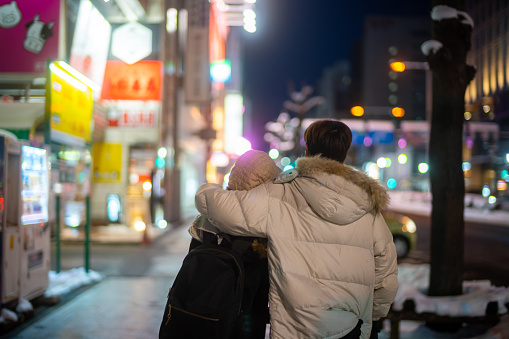 Happy Asian couple couple dating and shopping at retail store street market together in the city at night. Man and woman enjoy and fun outdoor lifestyle nightlife walking city street in winter night.