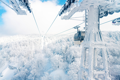 Point of view cableway moving up to snowy mountain peak ski resort. \nAerial view of pine tree forest mountain covered in snow under cable car. Ski lift transportation and winter travel vacation concept.