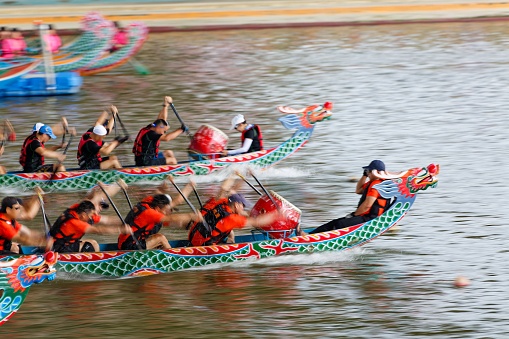 Scene of a competitive boat racing in the Dragon Boat Festival in Taipei, Taiwan, with view of athletes pulling vigorously on the oars and competing strenuously in traditional colorful dragon boats
