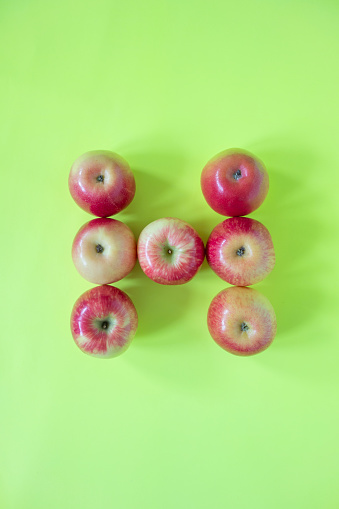 Red apples on green background forming “H” letter
