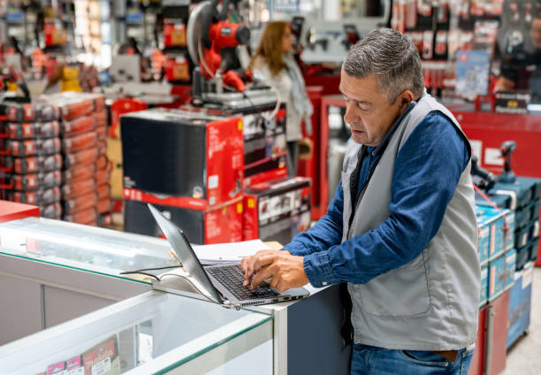 business manager working at a hardware store and making a call while using a computer - loja de ferragens imagens e fotografias de stock