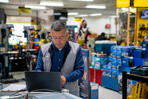 Portrait of a Latin American man working at a hardware store using a laptop computer
