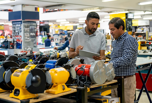 Latin American retail clerk helping a man shopping for a drill at a hardware store â small business concepts