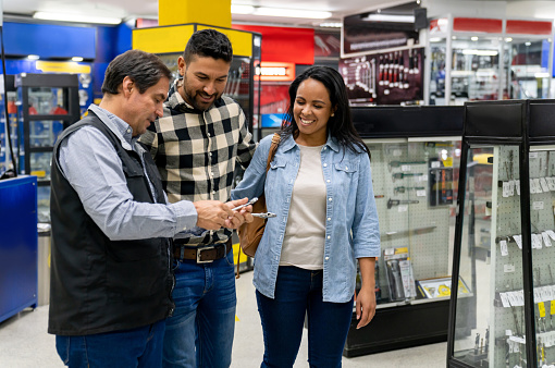 Latin American salesman helping a couple buying tools at a hardware store â small business concepts