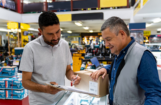 Latin American man delivering a package at a hardware store and asking for a signature from the owner