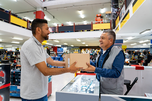 Happy Latin American delivery person picking up a package at a hardware store - e-commerce concepts