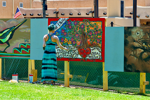 Taos, New Mexico, USA - July 24, 2023: A woman applies water sealant to freshly-painted artwork by artist Julie Terrell that is part of the Paseo Project to beautify Taos Plaza during its renovation by creating a temporary mural with the collaboration of 12 local artists.