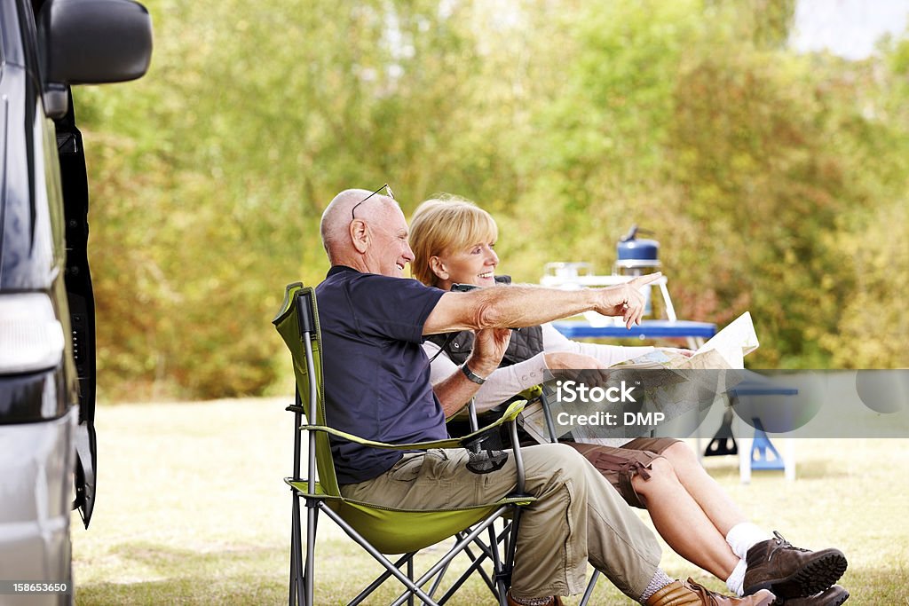 Senior couple sitting by camper van reading a map Relaxed senior couple sitting by camper van reading a map for directions Motor Home Stock Photo