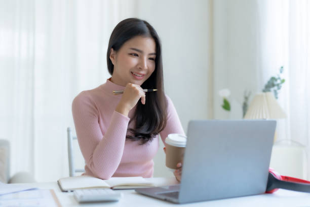 istock Smiling happy asian businesswoman sitting with laptop computer taking notes in office. 1586576745
