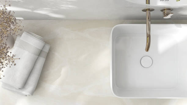 Cream marble vanity counter top, white modern rectangle ceramic washbasin, chrome faucet, flower vase, towel in bathroom in sunlight, shadow