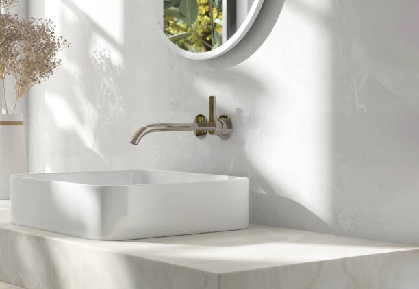 istock Cream marble vanity counter top, white modern rectangle ceramic washbasin, chrome faucet, flower vase in bathroom in sunlight and shadow 1586618699
