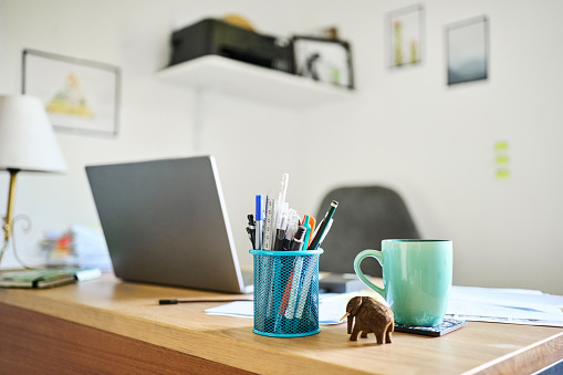 Simple home office setup with pen stand, elephant figurine, coffee cup and laptop on table