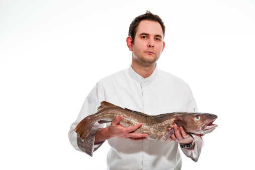 Young male cook with white jacket holding a big fish isolated on white.