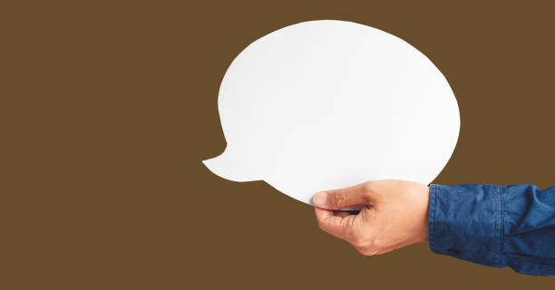 istock Close-up of hand holding a white speech bubble against a brown background 1586655185