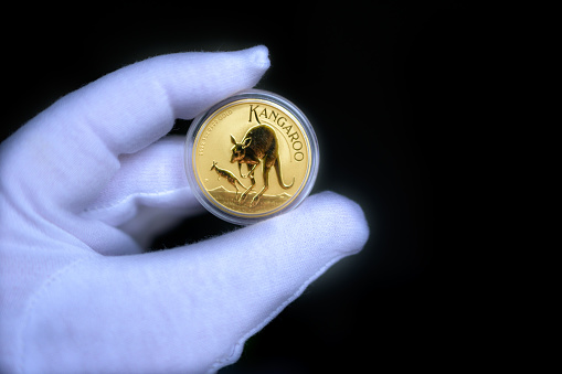 A gloved hand holding a one ounce gold coin with a kangaroo in a plastic sleeve