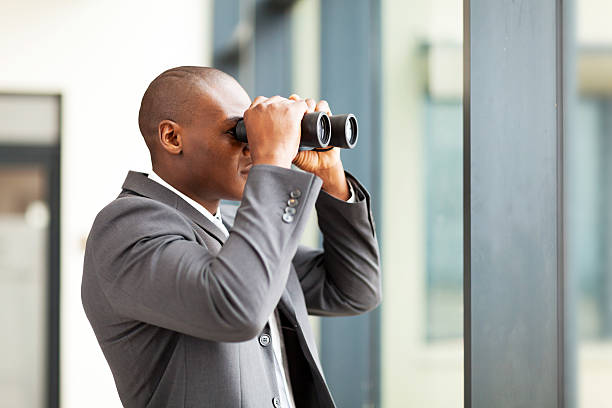 determined african american businessman using binoculars stock photo