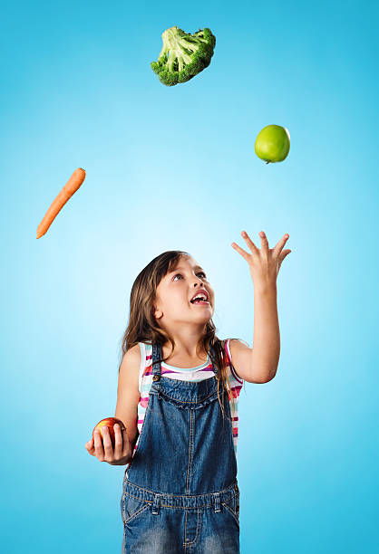 Young cute girl juggling vegetables and fruit over her head, healthy lifestyle, eating and diet concept