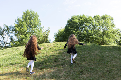 Two Happy Real Girls, Sisters in Dress Run Up The Hill In Summer. Joyful Children Spend Time in Nature, Park. Blue Sky on Horizon. Freedom Lifestyle, Carefree Childhood. Horizontal Plane.