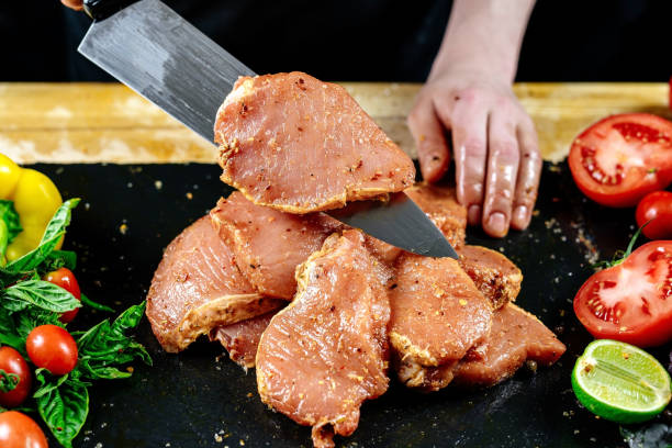 der küchenchef des restaurants bestreut fleisch mit gewürzen und mariniert es auf schwarzem hintergrund. marinieren von schweinefleisch zum grillen und schinken. - pork tenderloin dinner barbecue stock-fotos und bilder