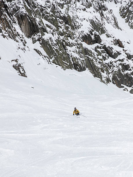 Man skiing powder snow below cliffs stock photo