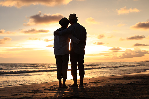 A couple of elderly walks relax and hug together beach against the sunset, Retirement lifestyle