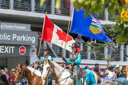 Calgary, Alberta, Canada. July 7, 2023.A couple of people riding horses holding a Canadian flag an Alberta flagat a public parade.