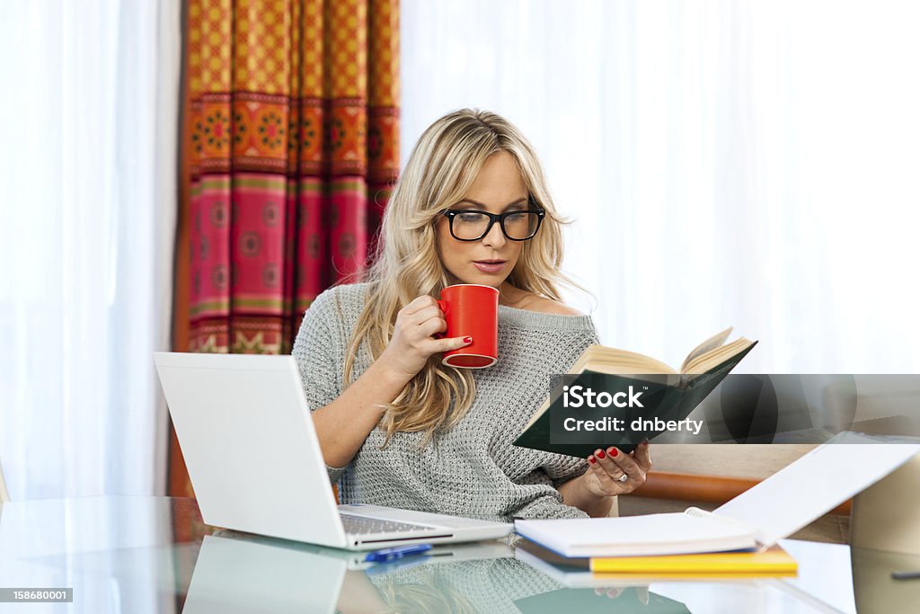 woman working on laptop at home attractive woman with cup of coffee, book and laptop sitting at her home desk and working Adult Stock Photo