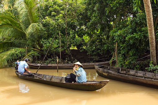 Ho-Chi-Minh,Vietnam, Asia- August 20,2023:Two Vietnamese drive on a wooden boat market in a side channel of the Mekong, Mekong Delta, Vietnam, Asia