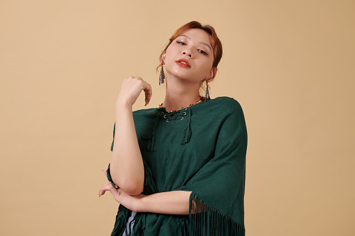 Portrait of young transgender woman in teal poncho standing against yellow background