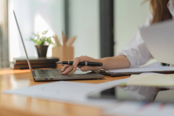 istock Close-up hand Asian woman holding a pen using a laptop. 1586894825