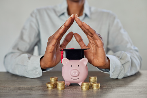 Close up of businesswoman hands showing sign of protection for graduation savings on piggy bank. African woman saving money for children education. Student loan, education savings and scholarship concept.