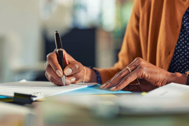 African business woman hand writing on paper at desk Close up of african american business woman hands writing on report while working in office. Successful black woman signing documents at home using a pen. Mid adult freelancer signing contract document on table. handwritten signatures stock pictures, royalty-free photos & images