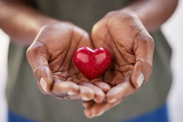 Close up of black woman hands holding a small red heart. Small heart in the hands of a african woman. Solidarity, charity and responsibility concept.