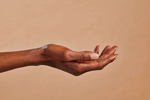 Close up of african american woman hand with palm facing upwards isolated on brown background. Female black hand showing empty hand. African girl holding your beauty product.