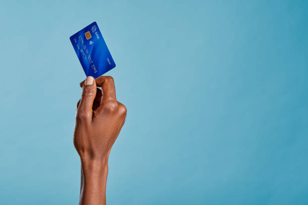 파란색 배경에 분리된 신용 카드를 들고 있는 흑인 여성 손 스톡 사진