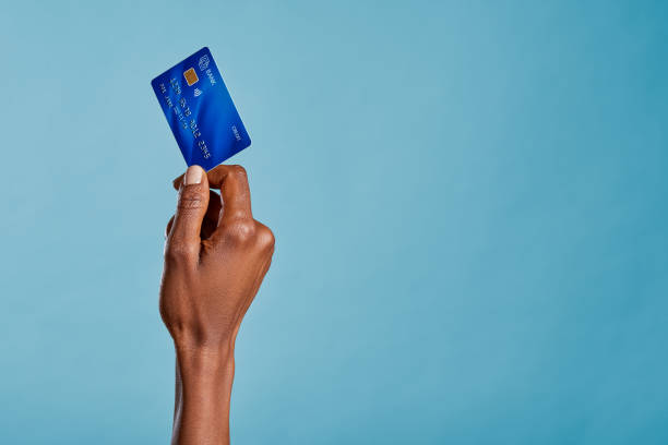 Black female hand holding credit card isolated on blue background stock photo