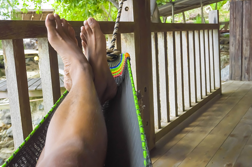 Photo of someone's feet relaxing in a hammock by the beach at a tropical Piugus Island Resort, Anambas, Riau Archipelago, Indonesia. Someone is sleeping in a hammock in a tropical island villa.